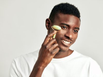 Black guy with youthful skin using jade de-puffing face roller to keep his skin soft and smooth Black guy with youthful skin using jade de-puffing face roller to keep his skin soft and smooth
